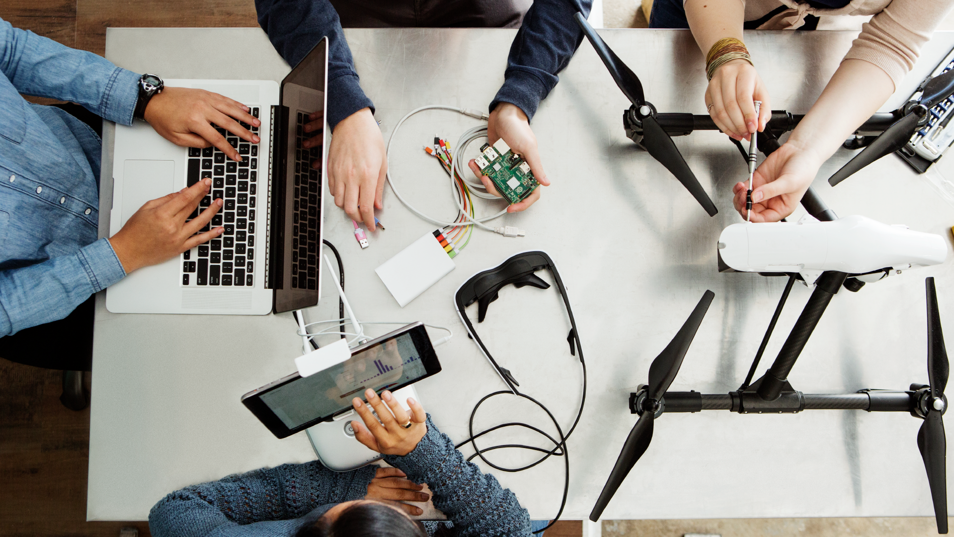 A group of people sitting at a table using a laptop and a tablet to build a drone.